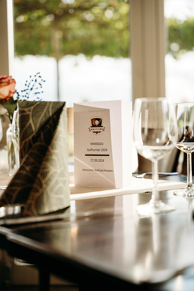 Tischdekoration mit MAKRADU Golfturnier 2024 Menükarte und eleganten Weingläsern auf dem Event im Märkischen Golfclub Potsdam. Business-Golfevent mit gehobener Atmosphäre und hochwertigen Details für die Teilnehmer.